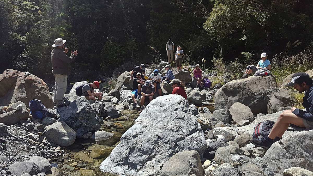 Group of students on riverbed listening to tutor
