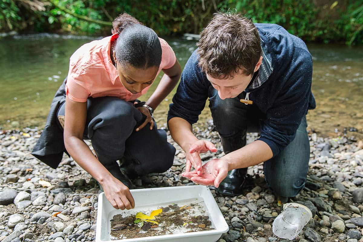 Two environmental science students looking at samples by river